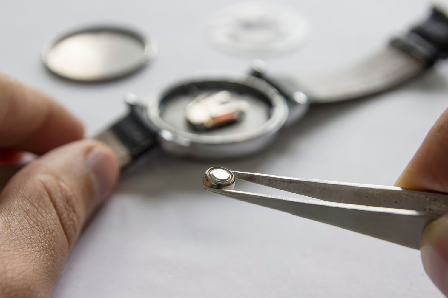Watchmaker holding a new watch battery with tweezers during service