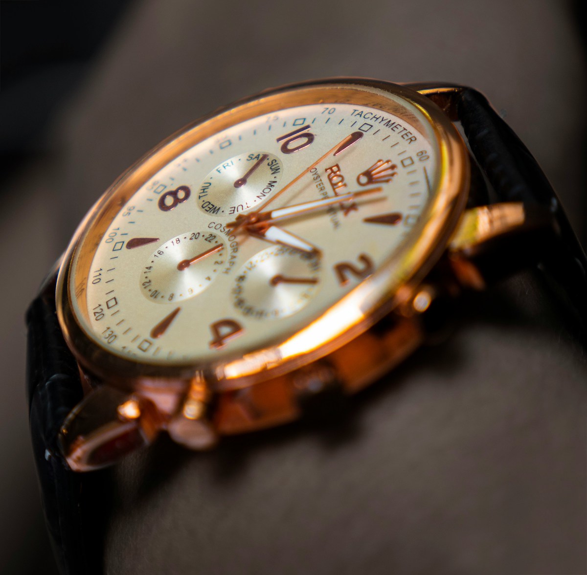 Gold Rolex chronograph with a cream dial on a dark leather strap